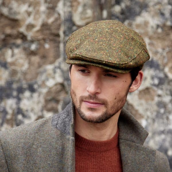 Man wearing a green tweed flat cap against a stone wall background