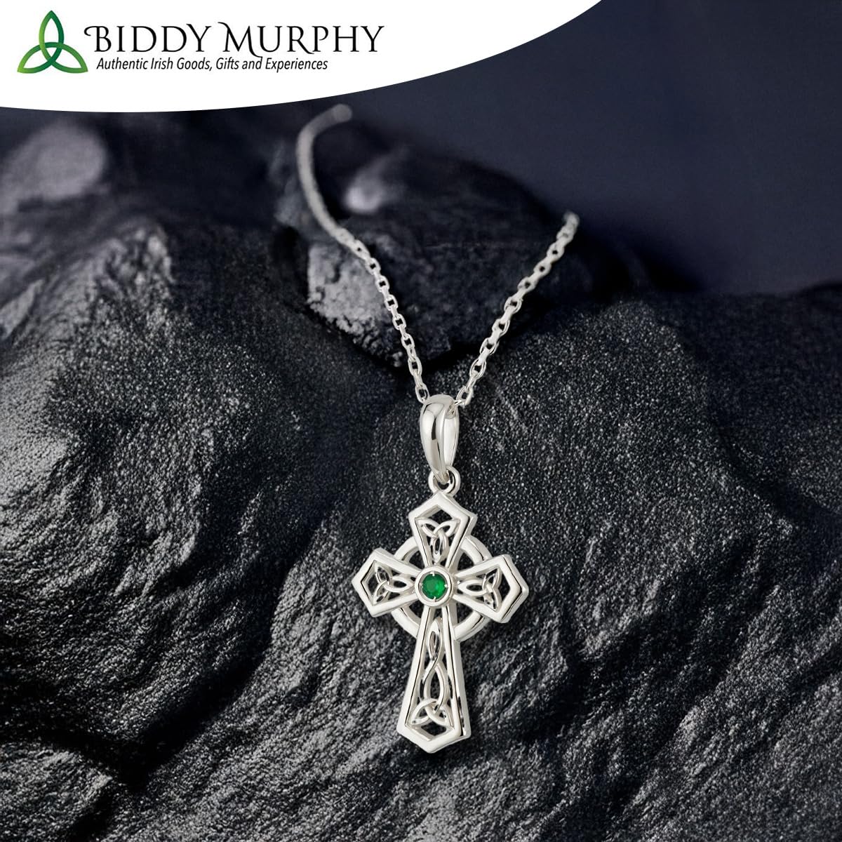 Silver cross pendant with a green gemstone on a dark stone surface, featuring Biddy Murphy branding.