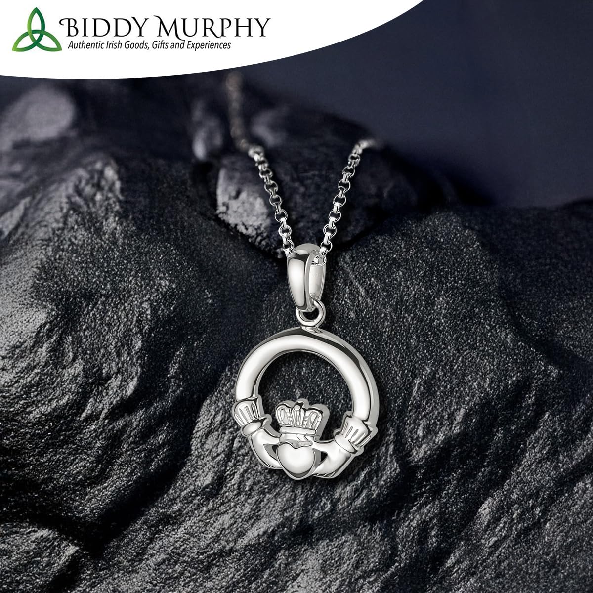 Silver Claddagh pendant on a dark stone surface with Biddy Murphy branding.