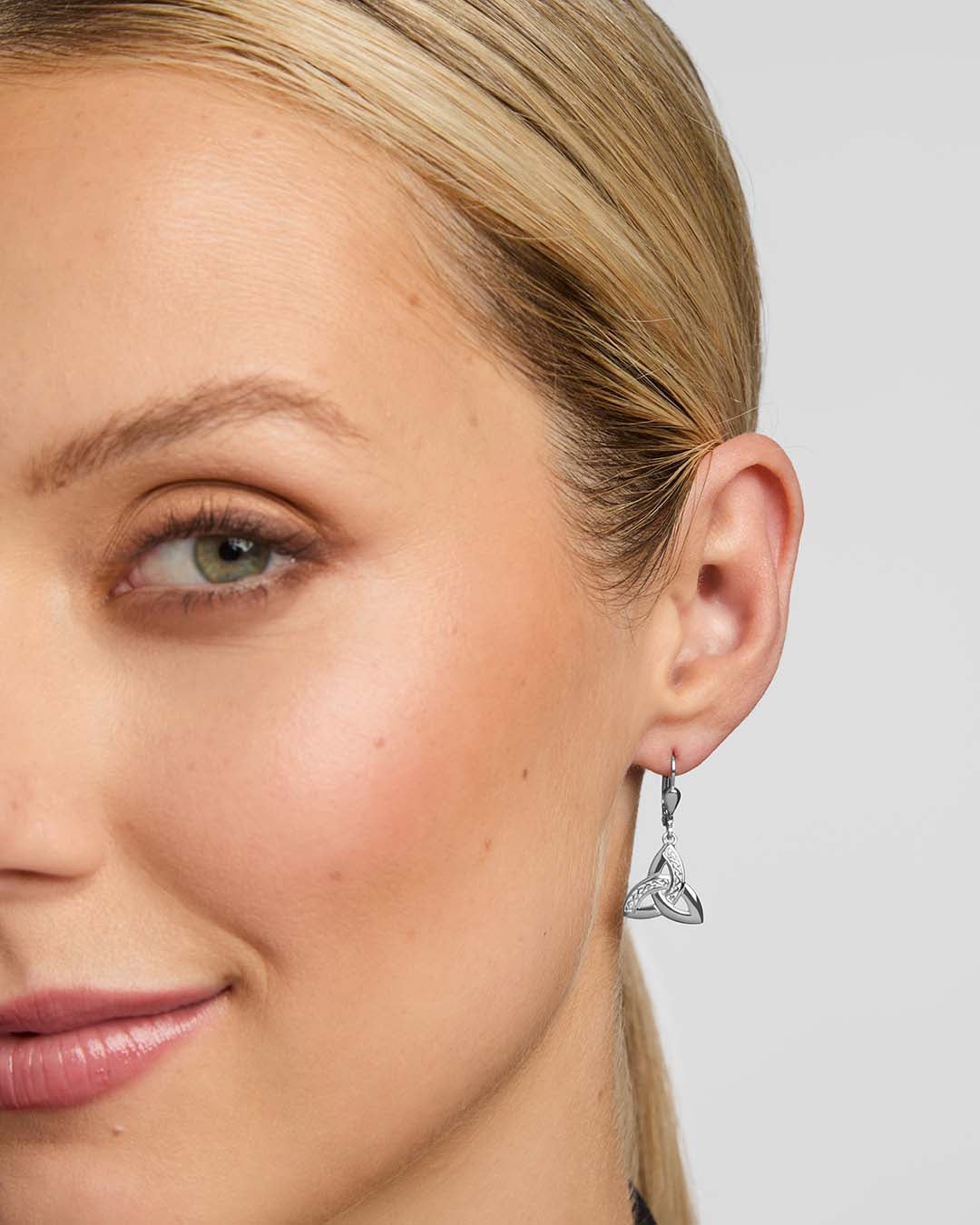Close-up of a woman wearing a silver triangle earring against a neutral background