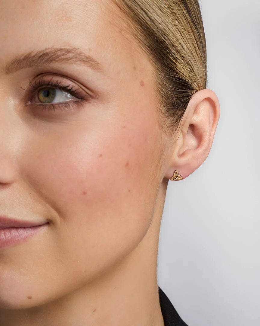 Close-up of a woman wearing a gold heart-shaped earring against a neutral background